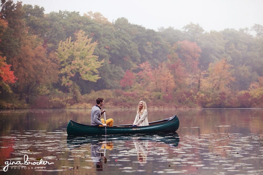 A couple float down the charles river in a canoe during their cozy fall engagement session in boston