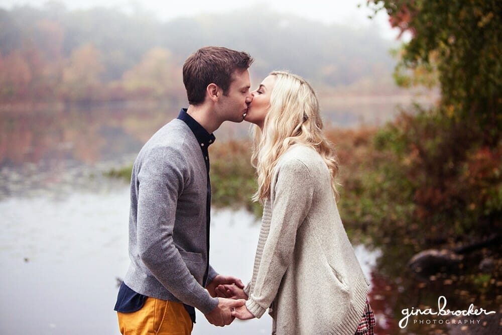 A couple kiss romantically against a misty fall backdrop of the charles river in boston.