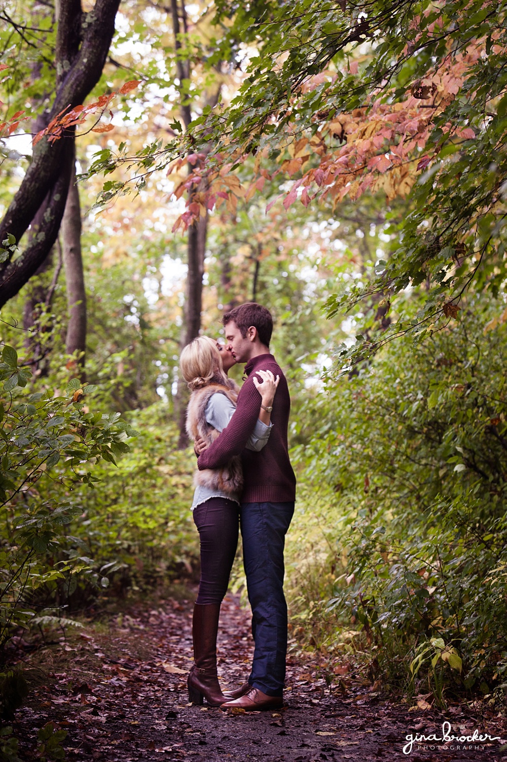 A couple share a kiss in the woods during their woodsy fall engagement session in massachusetts