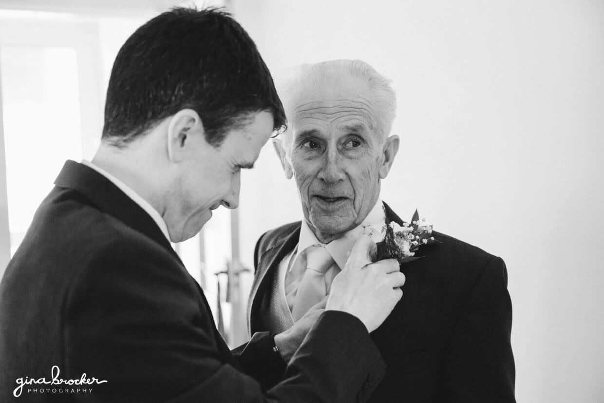 The groom puts a boutonniere on his father during the morning of a vintage inspired wedding