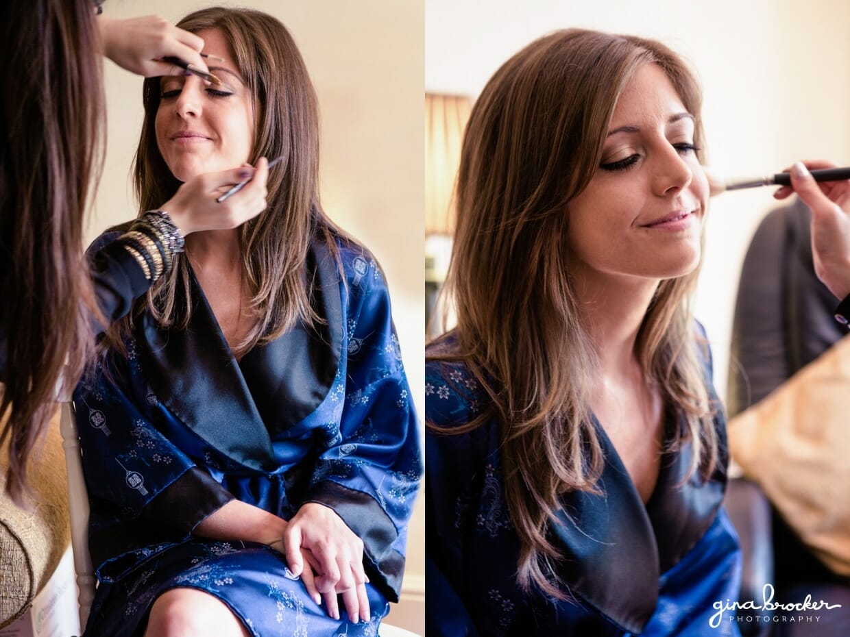 bride wears a blue silk robe while getsing her makeup done on the morning of her elegant wedding