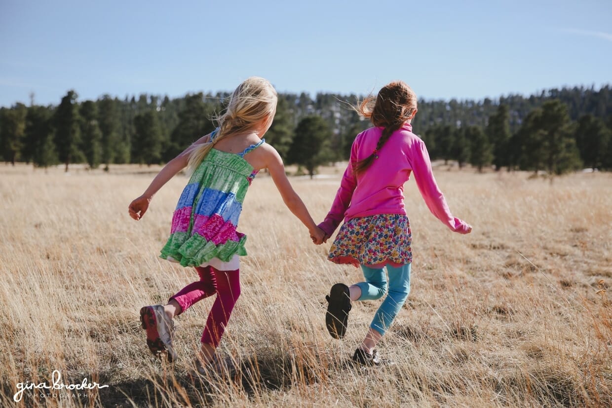 Two sisters hold hands as the run into the field during their outdoor photography session