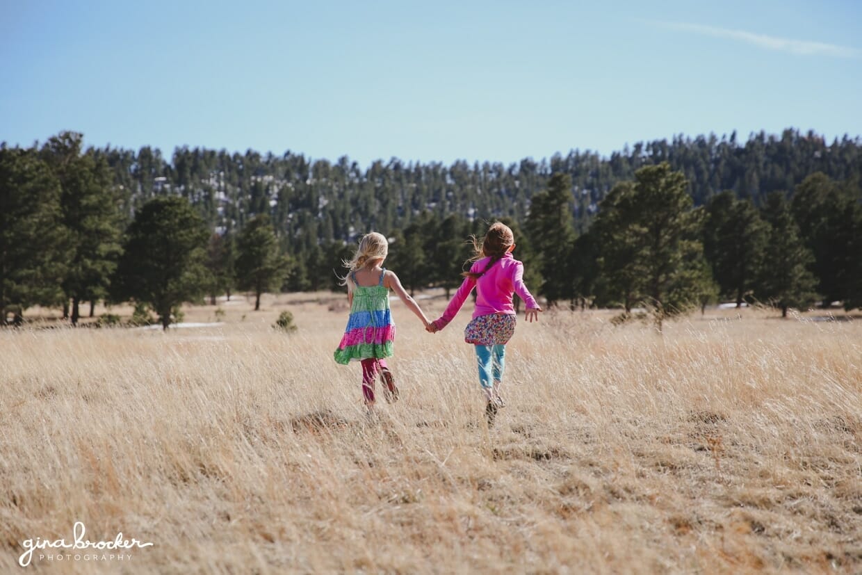Two sisters hold hands and walk in a field during their lifestyle photography session