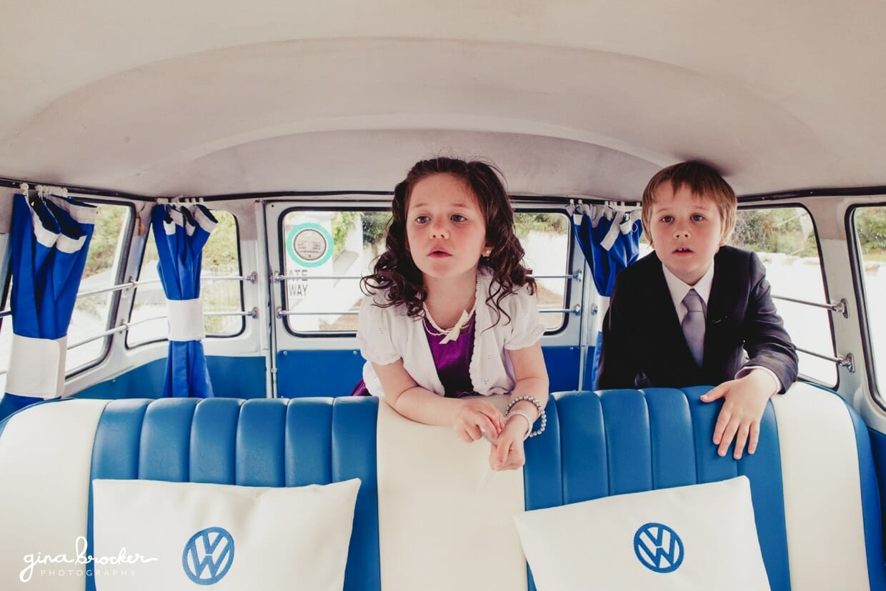 A flower girl and ring bearer wait for the wedding party in a blue volkswagen bus on the morning of a retro wedding