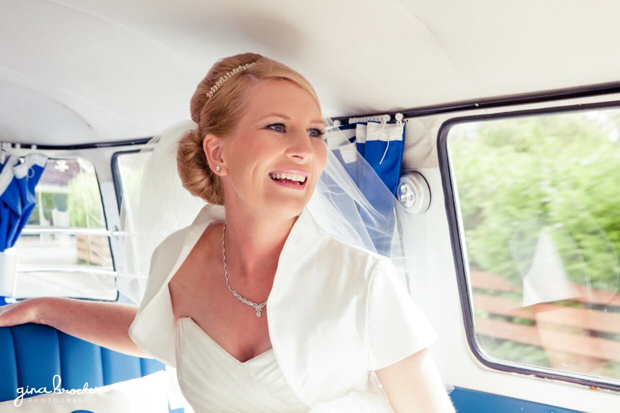 A bride smiles on the way to the church in a blue retro volkswagen bus