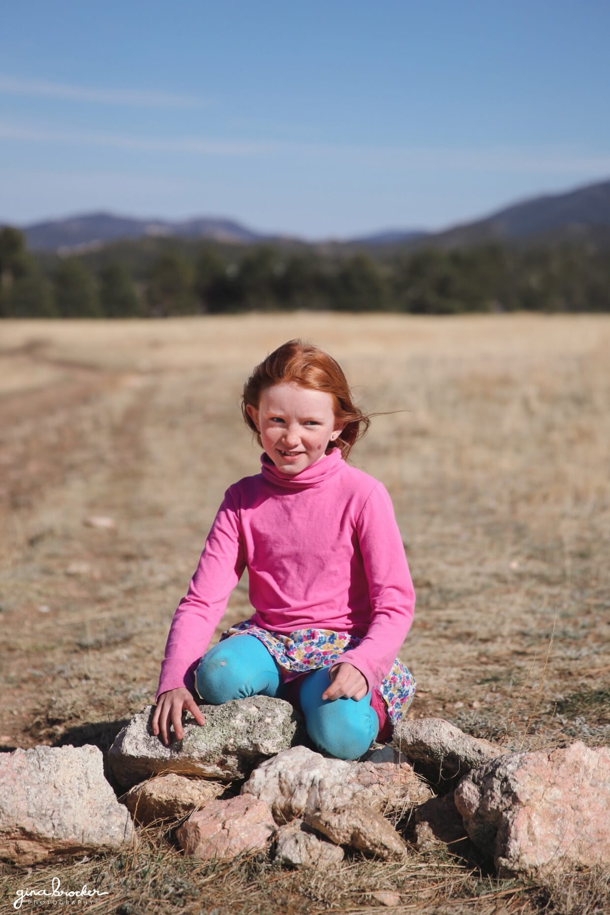 portrait of a young girl sitting on a rock in a field