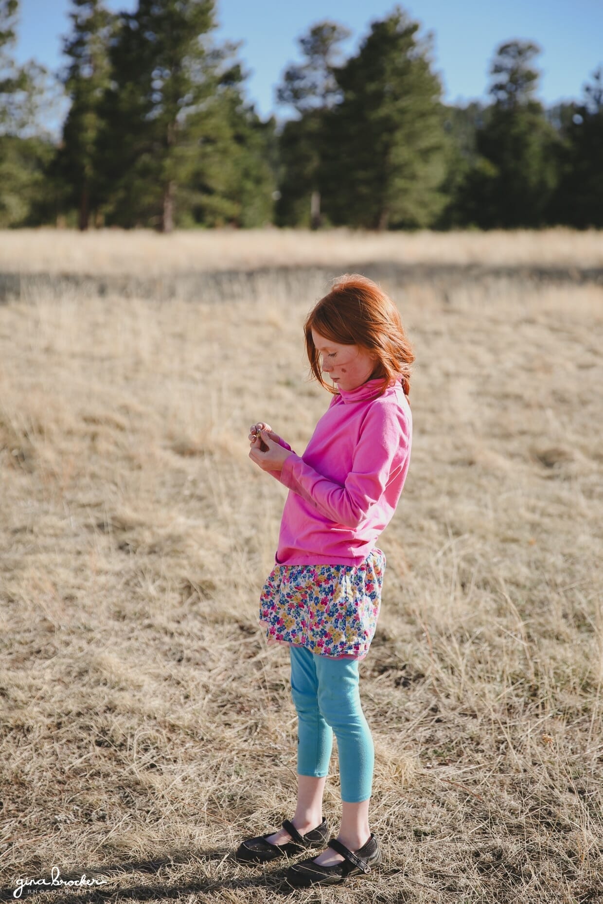 A young girl looks at a flower in her hand while standing in a field