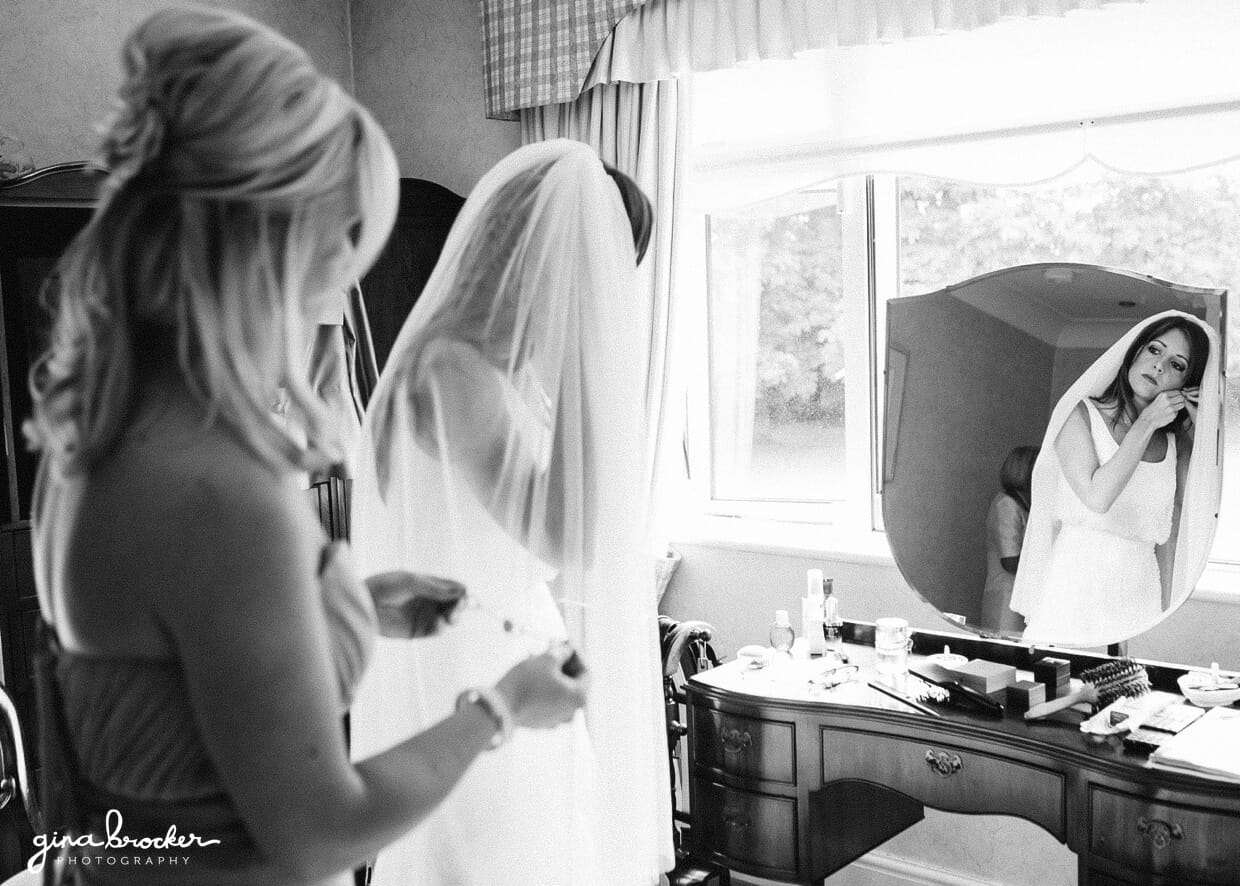 A photojournalistic wedding photograph of a bride looking in the mirror while putting on her earrings