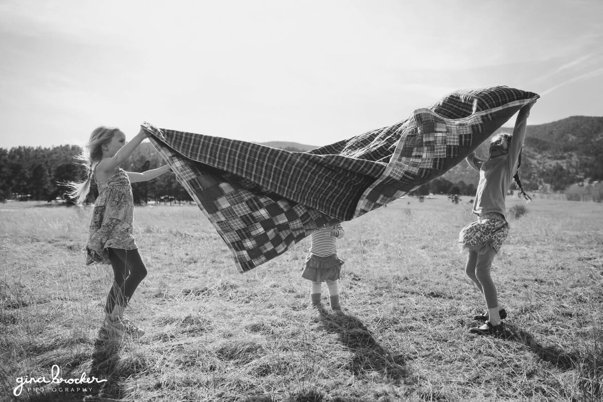 Three kids throw a blanket up in the air before laying it down on the ground