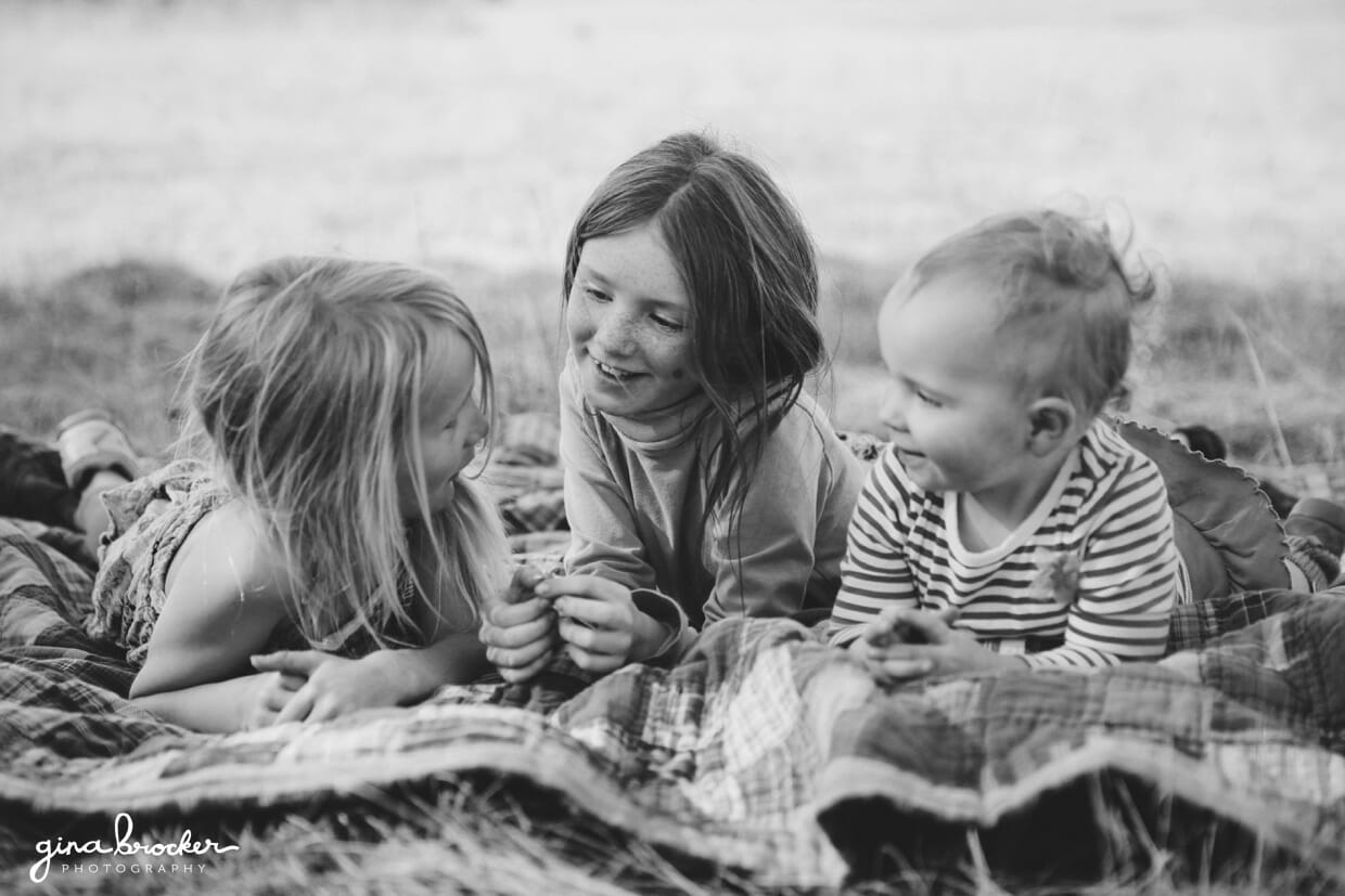 Three young girls lay on a blanket outside and talk during their natural family photo session
