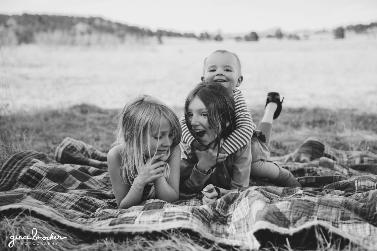 A natural and fun photograph of three sisters playing on a blanket during their family photo session in Boston, Massachusetts