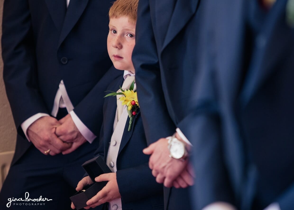 The ring bearer stands amongst the groomsmen while tightly holding the wedding rings 
