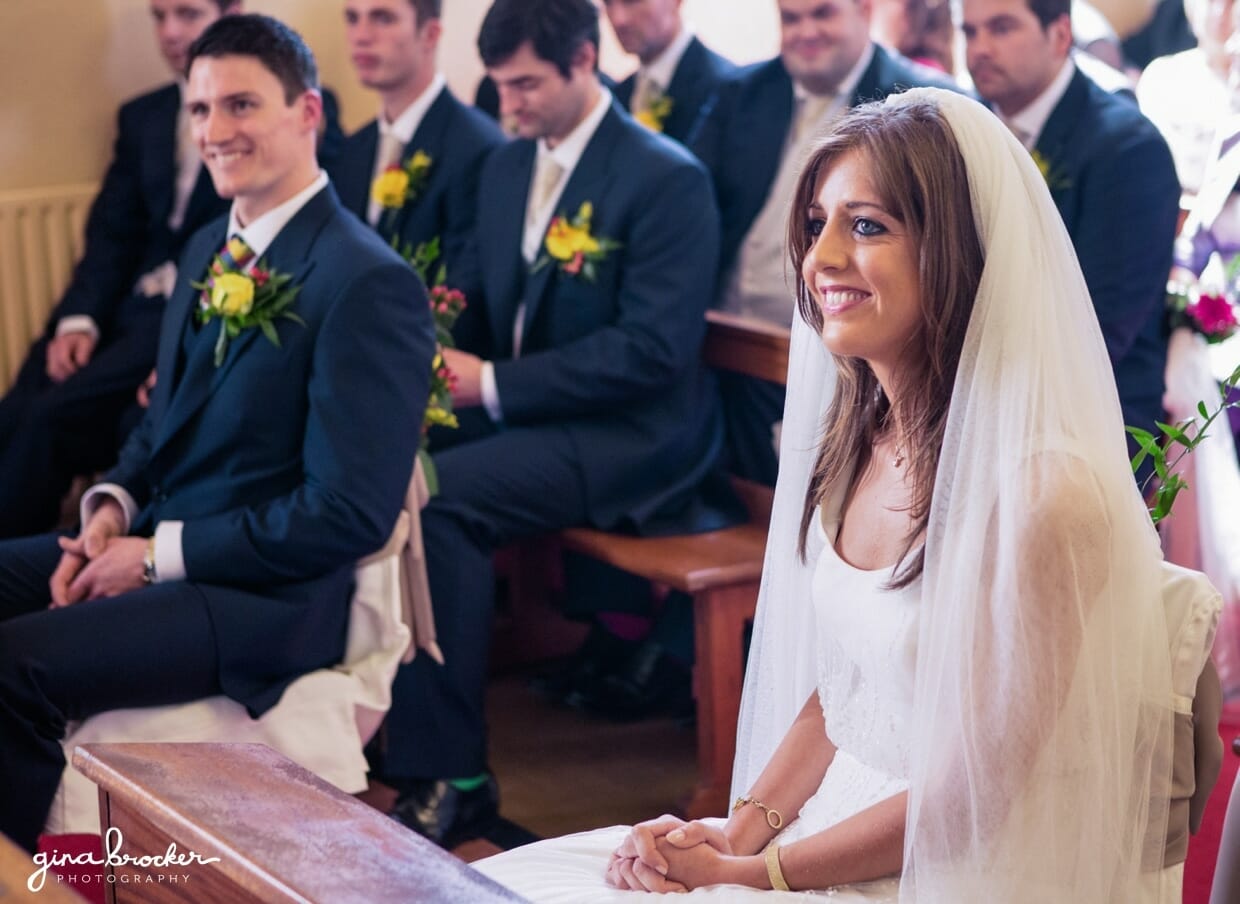 The bride and groom smile as their good friend reads a poem during their intimate wedding ceremony in a small church