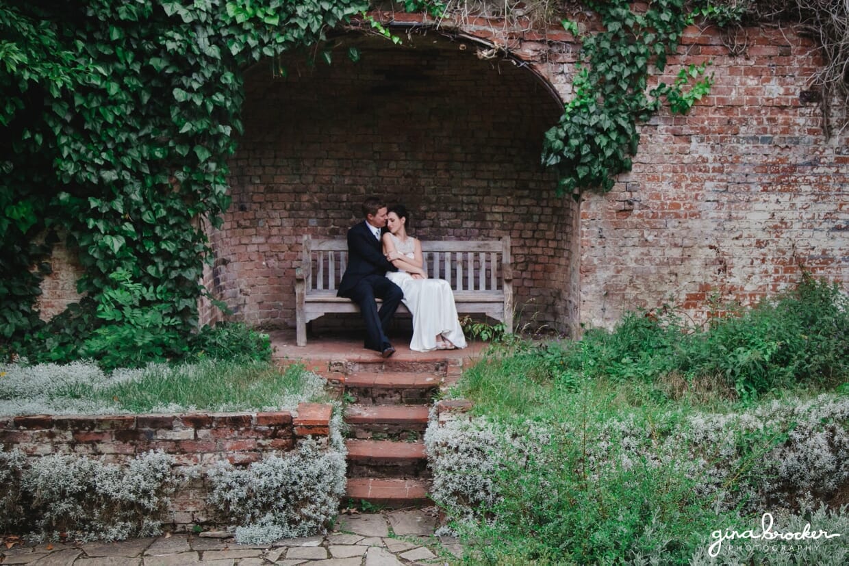 A wedding couple cuddle on a bench during their portrait session in a walled garden