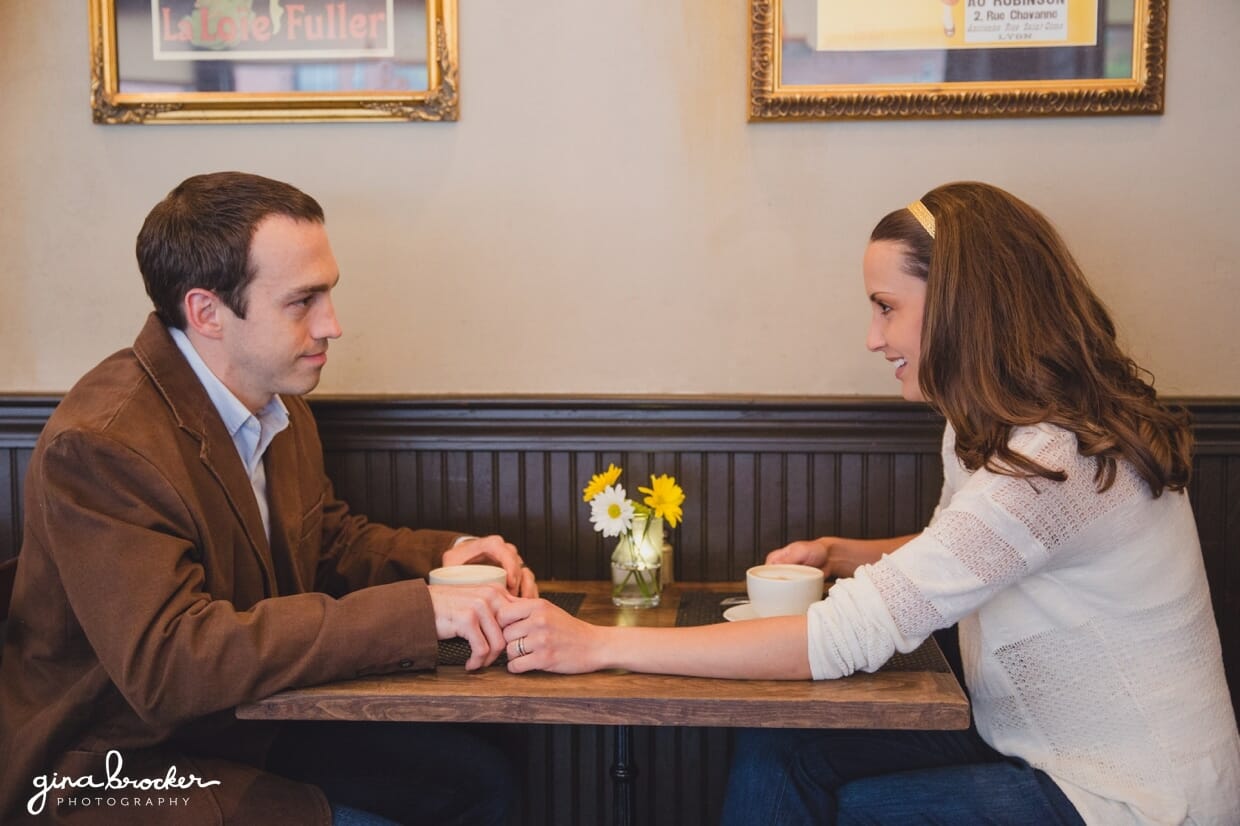 A couple hold hands across the table during their cafe couple session in beacon hill, Boston
