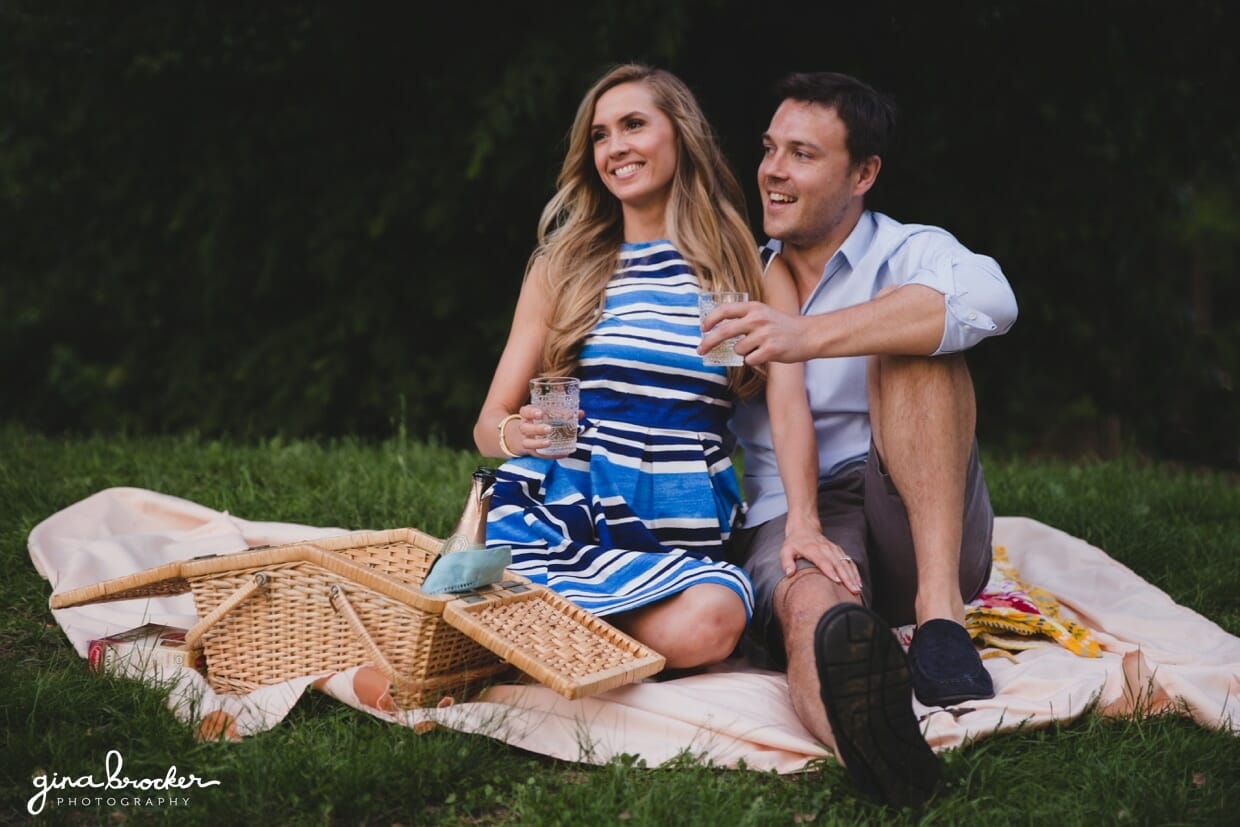 A couple laughs while they sit on a blanket during their picnic engagement session in prospect park, brooklyn, new york