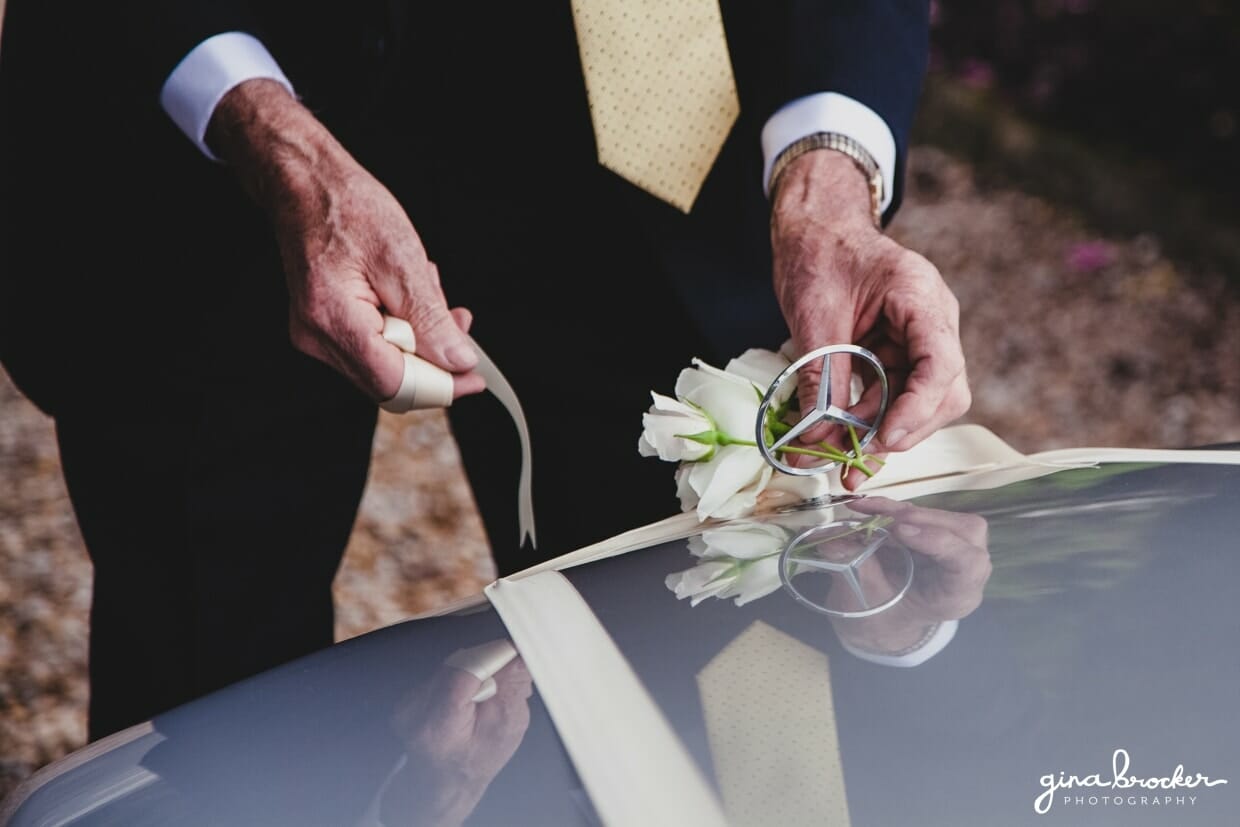The groom's father ties white roses to the wedding car on the morning of their classic garden wedding