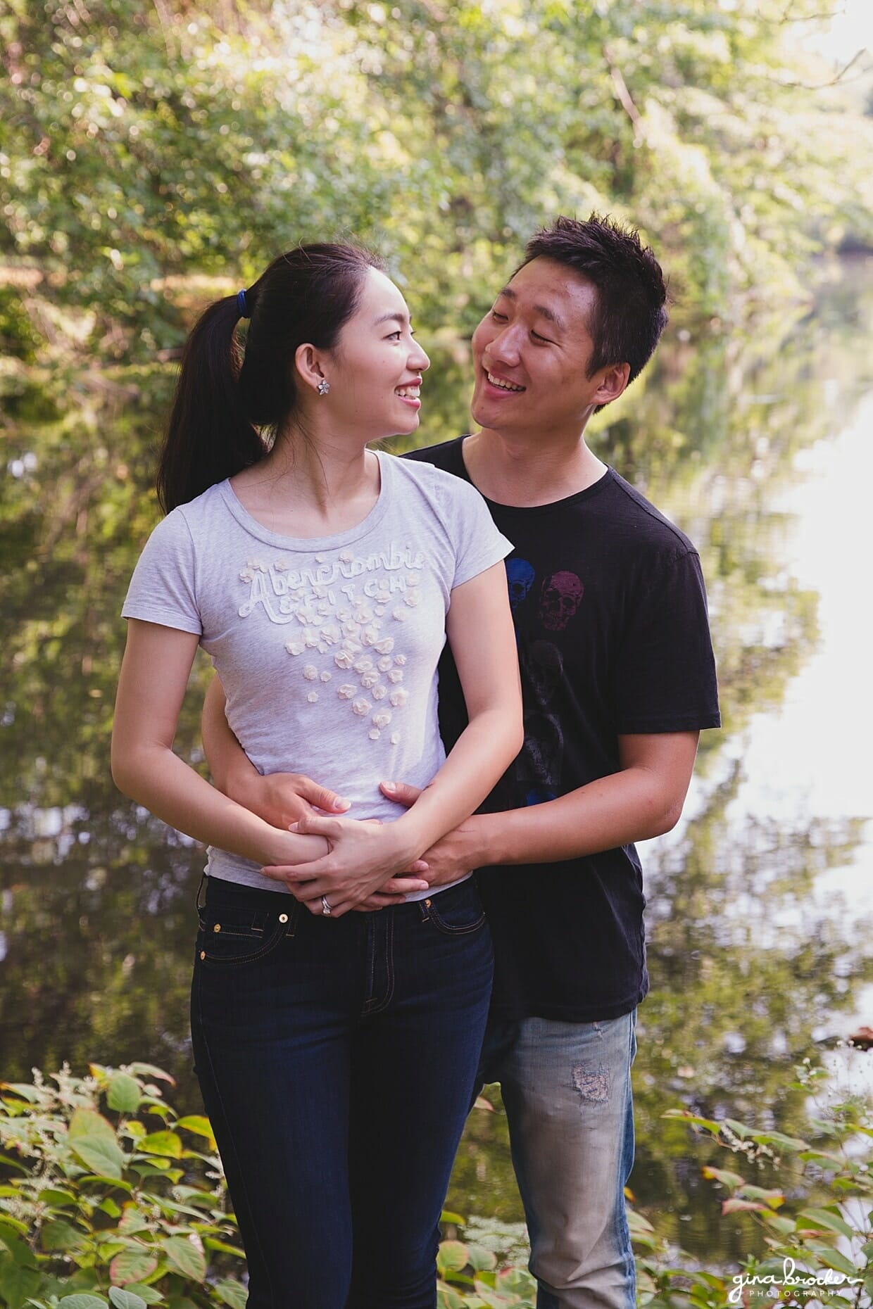 A couple laugh together by the water in back bay fens park during their Boston engagement session