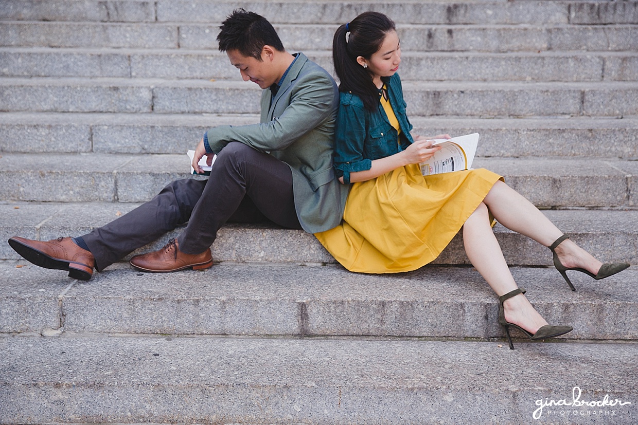 A couple sit back to back and read books on the steps of Northeastern University during their college themed engagement session in Boston, Massachusetts