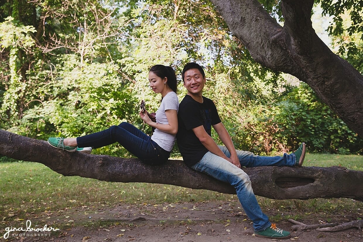 A couple play music together while they sit on a tree in Back Bay Fens during their park engagement in Boston, Massachusetts