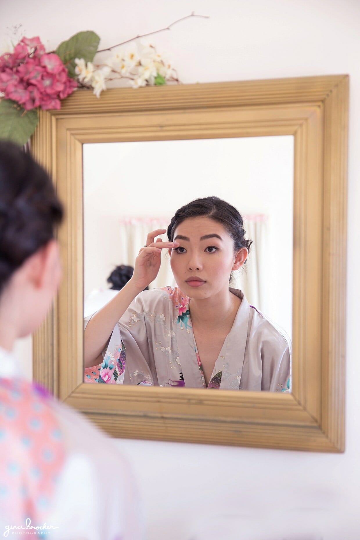A bride fixes her makeup in a mirror on the morning of her hammond castle wedding in gloucester, massachusetts