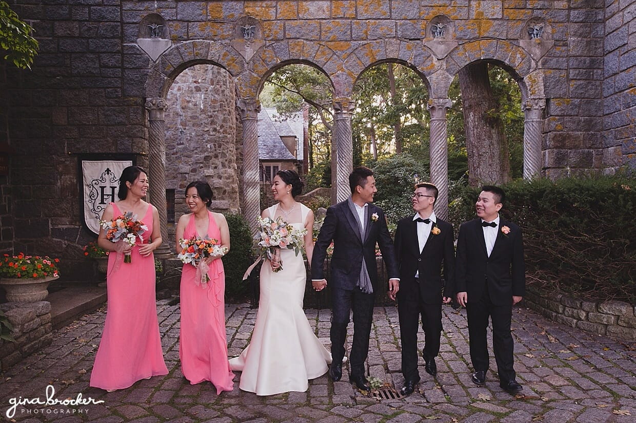 A natural photograph of a wedding party in pink and black walking together at Hammond Castle during a Gloucester wedding
