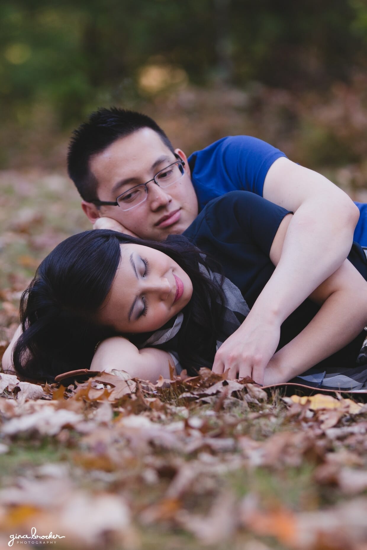 A couple lay together in the leaves during their fall engagement session in boston