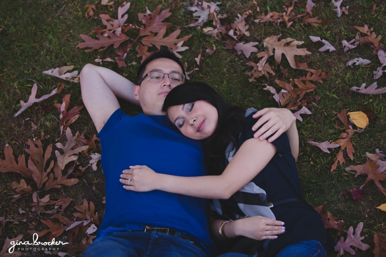 A couple lay amongst fallen leaves during their fall engagement session in boston 