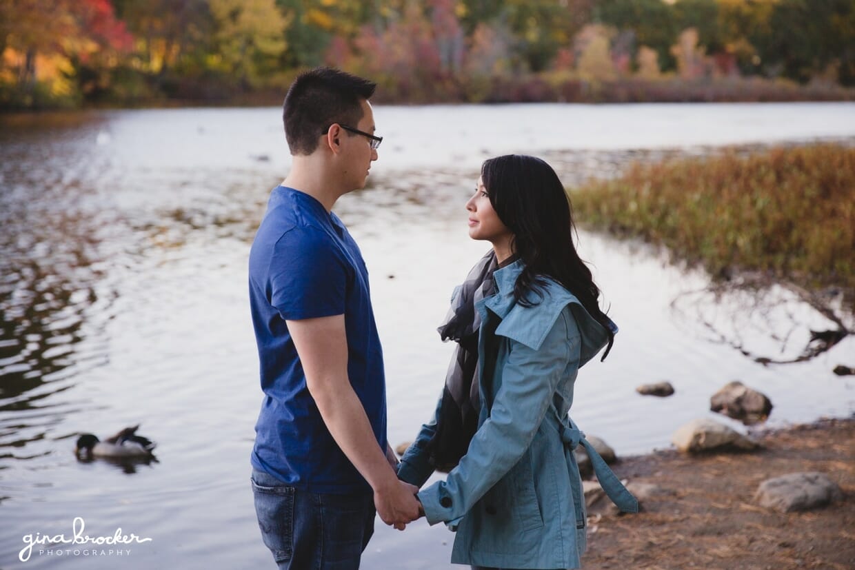 A couple hold hands while they stand together by the charles river during their fall engagement session in boston