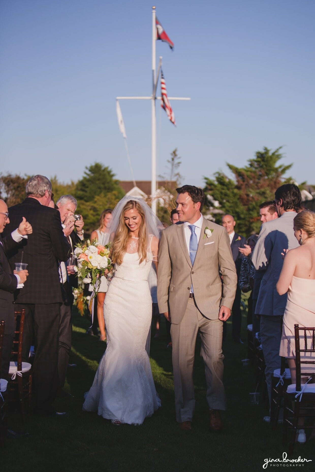 The bride and groom smile as they walk down the aisle together after their sunny outdoor wedding ceremony at the Westmoor Club in Nantucket, Massachusetts