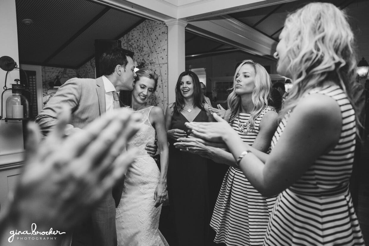 A fun photograph of the groom kissing his bride while the wedding party dance around them during their Nantucket wedding reception at the Westmoor Club