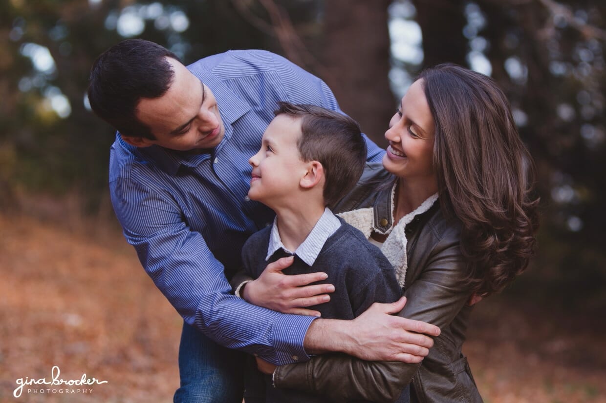 A mom and dad hug their son during their fall family photo session in Boston's Arnold Arboretum