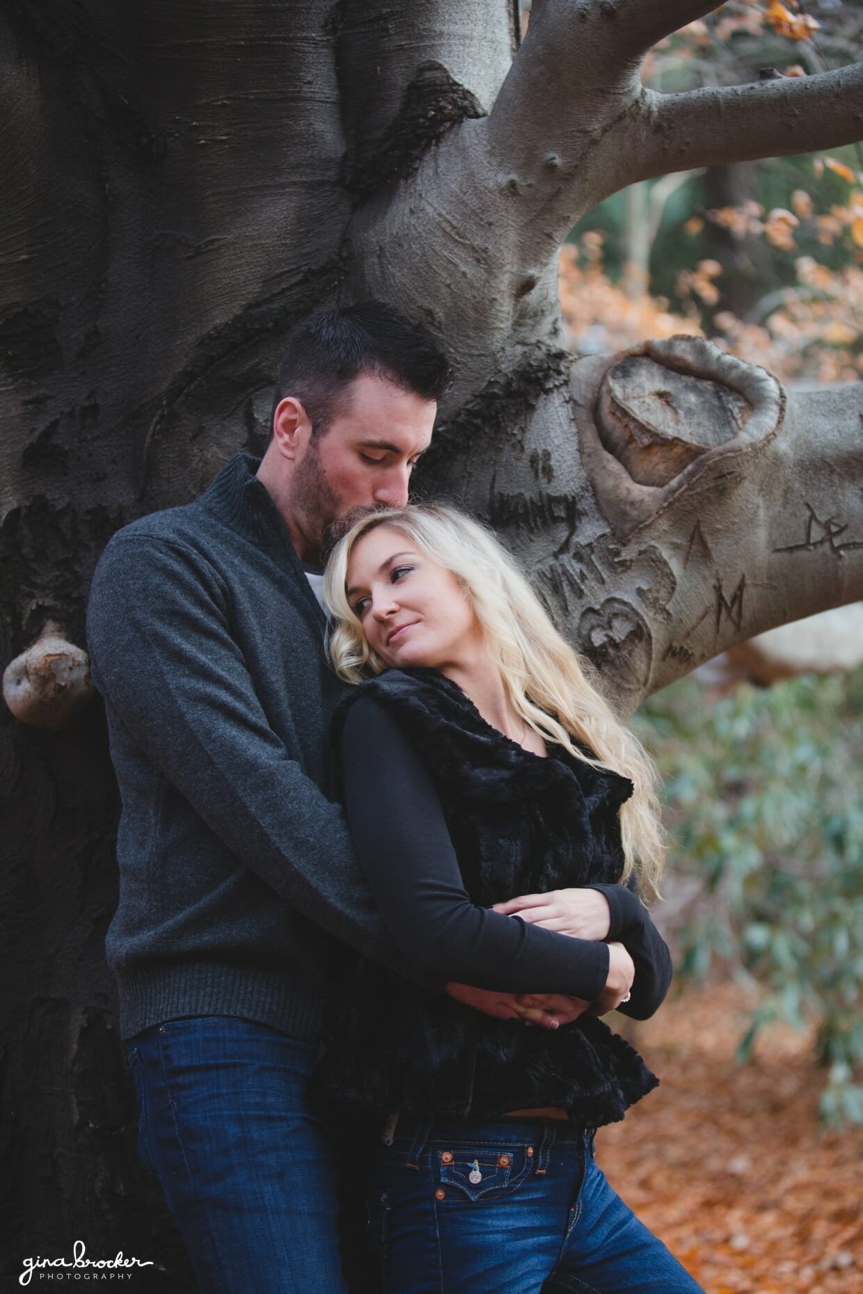 A couple cuddles against a tree in Arnold Arboretum during a fall couple session in Boston, Massachusetts