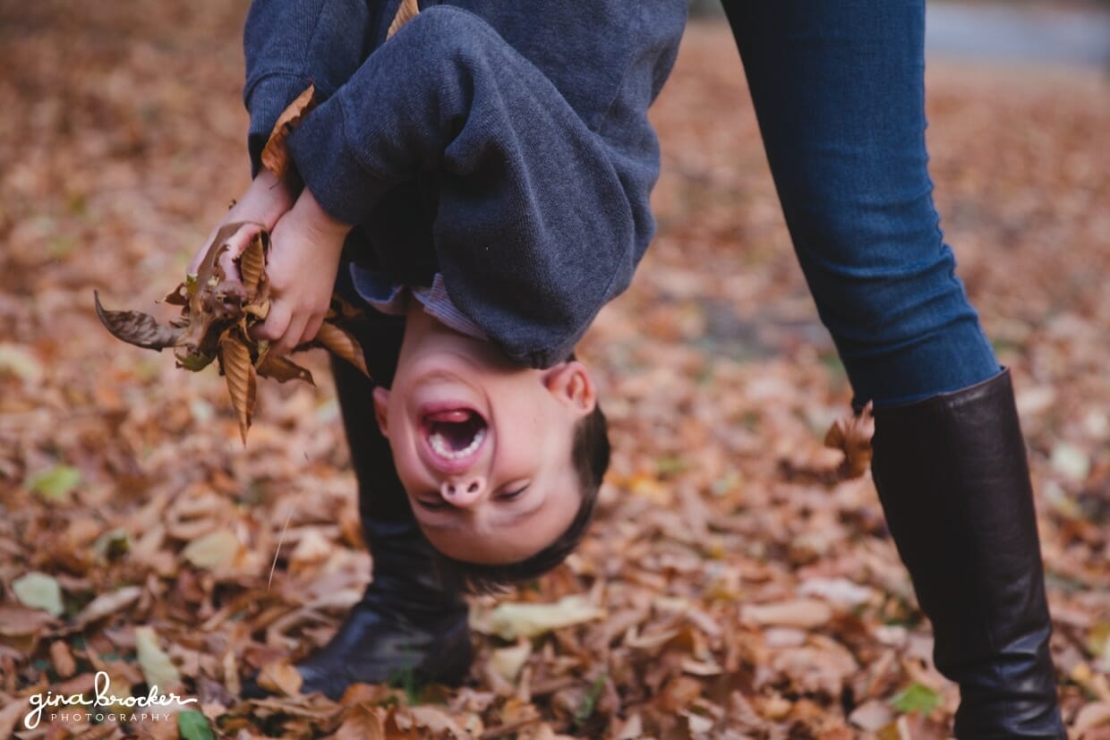 A fun photograph of kid playing with leaves with his mother during a natural and fun fall family photo session in Boston's Arnold Arboretum
