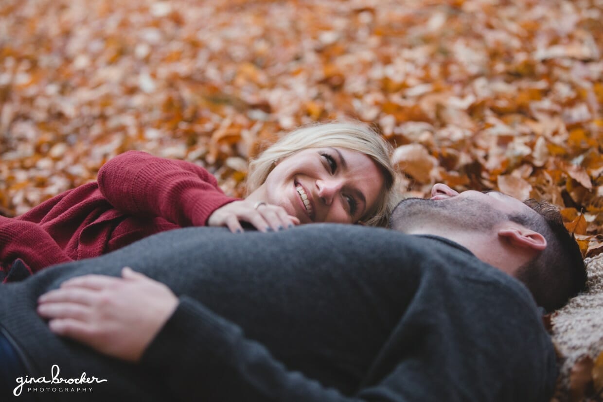 A sweet photograph of a couple laying together on a blanket in the fallen leaves during their fall couple session in Boston's Arnold Arboretum