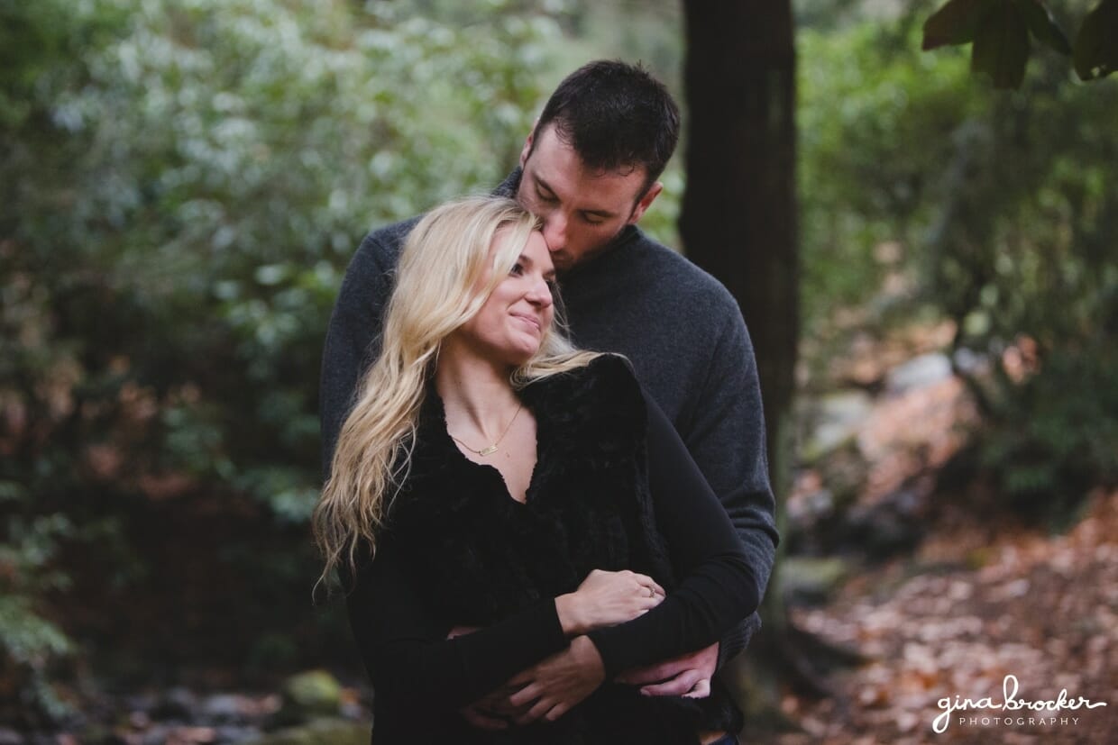 A sweet photograph of a couple cuddling in the woods during their fall couple session in Boston's Arnold Arboretum