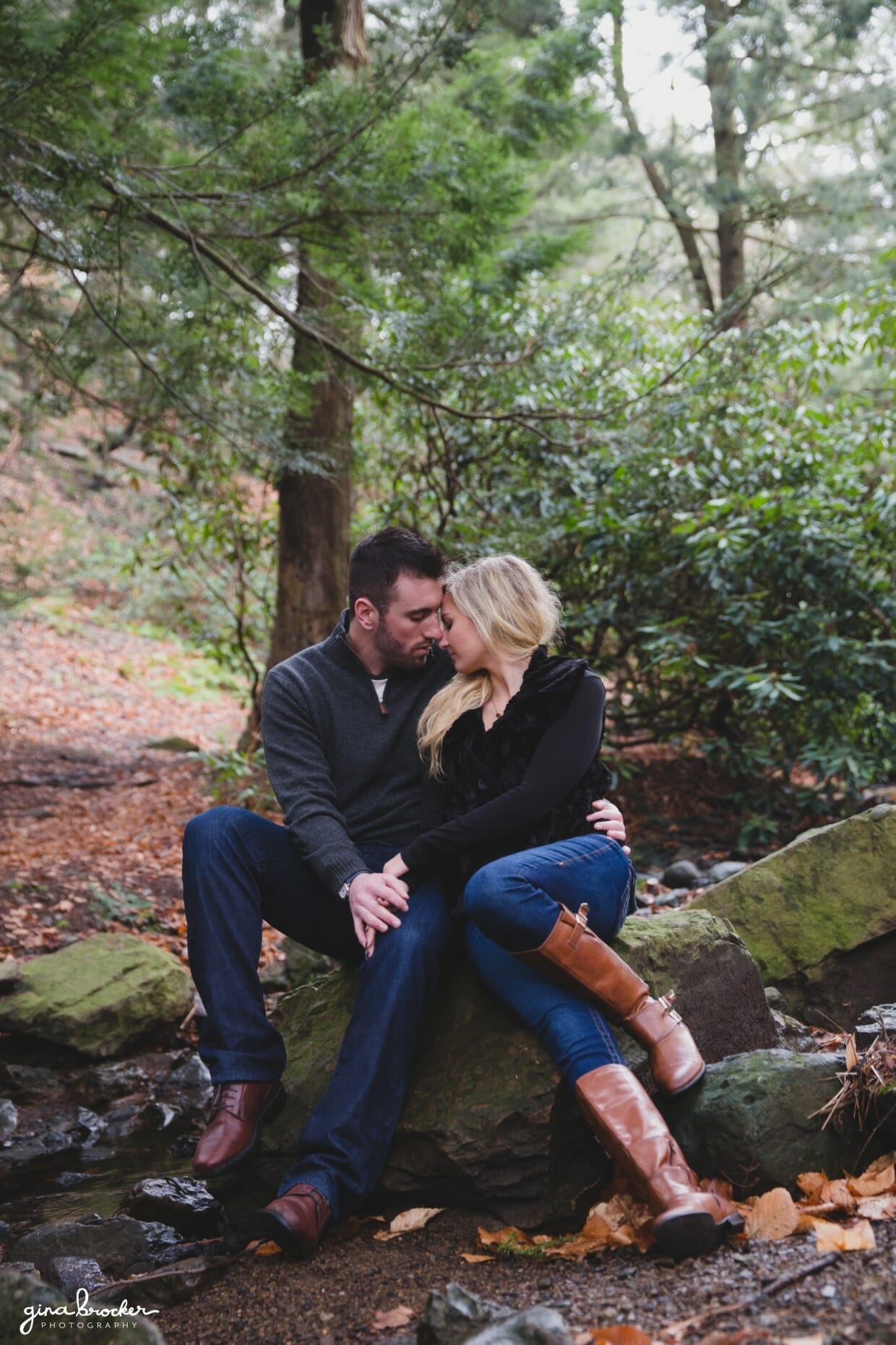 A beautiful photograph of a couple sitting together on a rock in the woods during their fall couple session at the Arnold Arboretum in Boston, Massachusetts