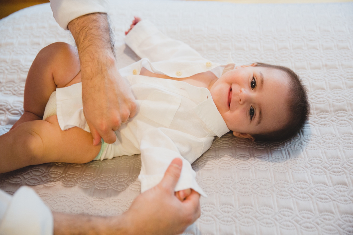 A cute baby boy smiles while being dressed during an in home family photo session in Boston. 
