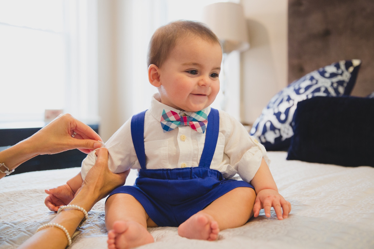 A baby boy smiles while getting dressed during a Boston family photo session at home.