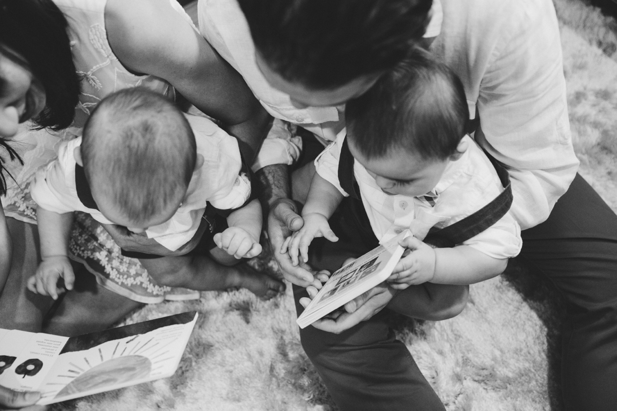 A documentary and artistic photograph of parents reading a story to their twin baby boys during their Boston family photo session at home.
