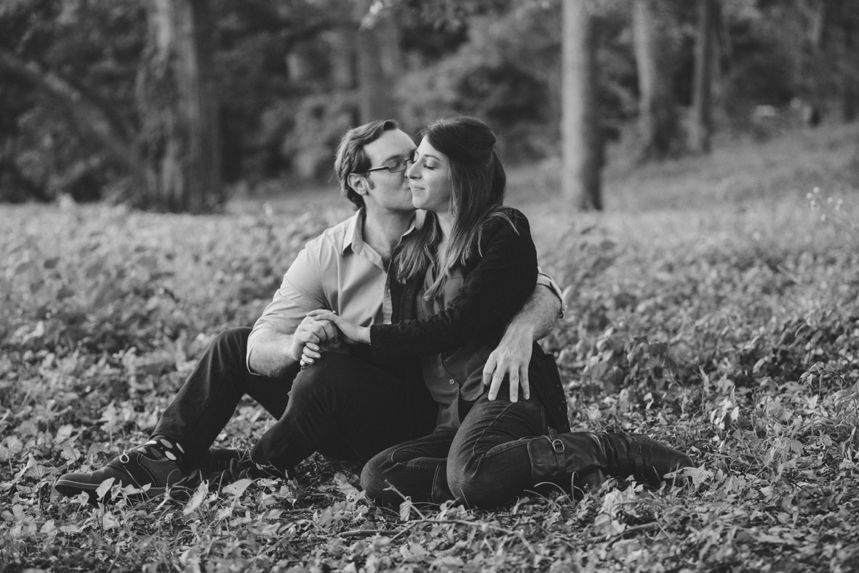 A romantic photograph of a couple cuddling in the grass during their Arnold Arboretum engagement session in Boston