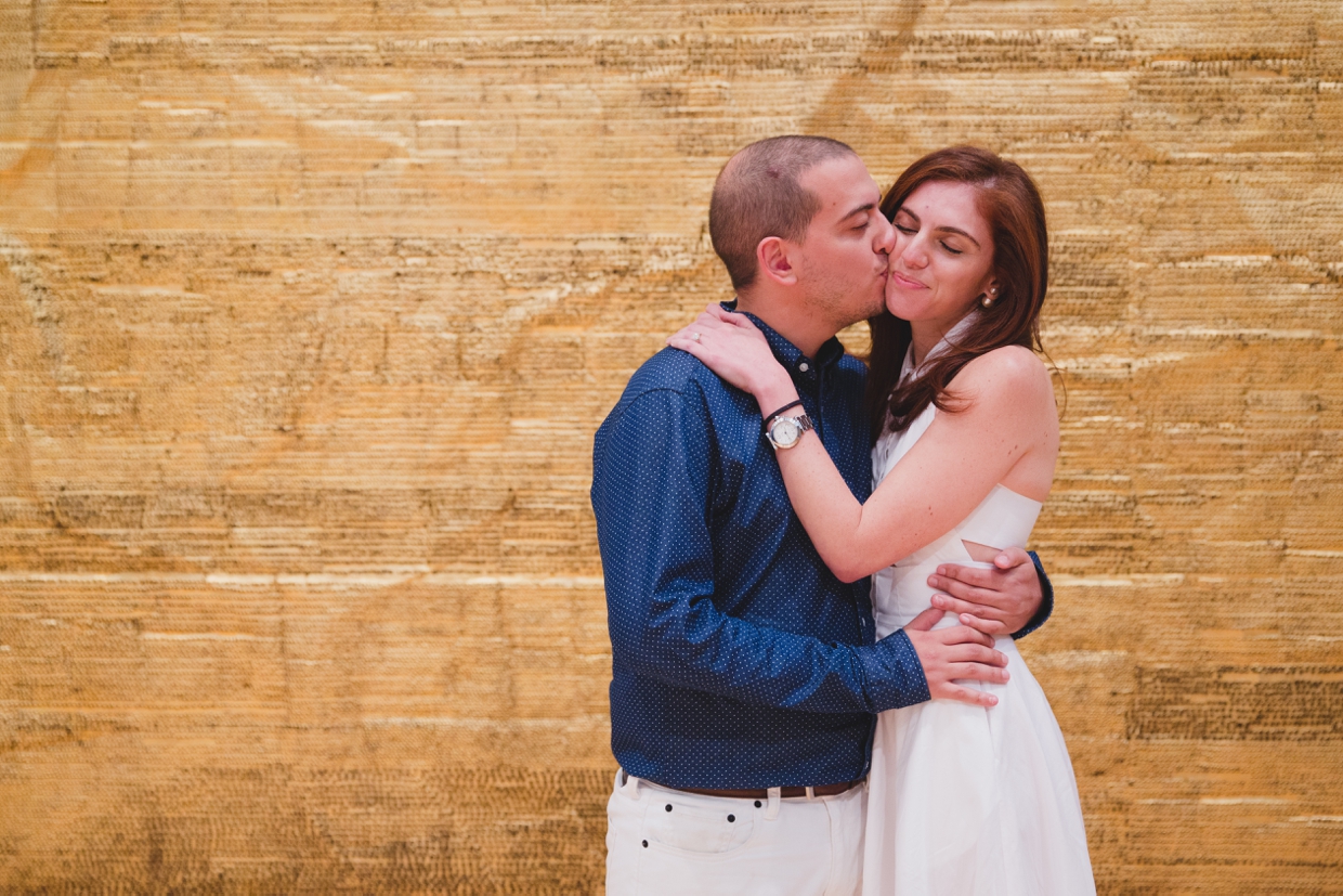 A couple hug and kiss in front of a contemporary gold painting during their engagement session at the Museum of Fine Arts