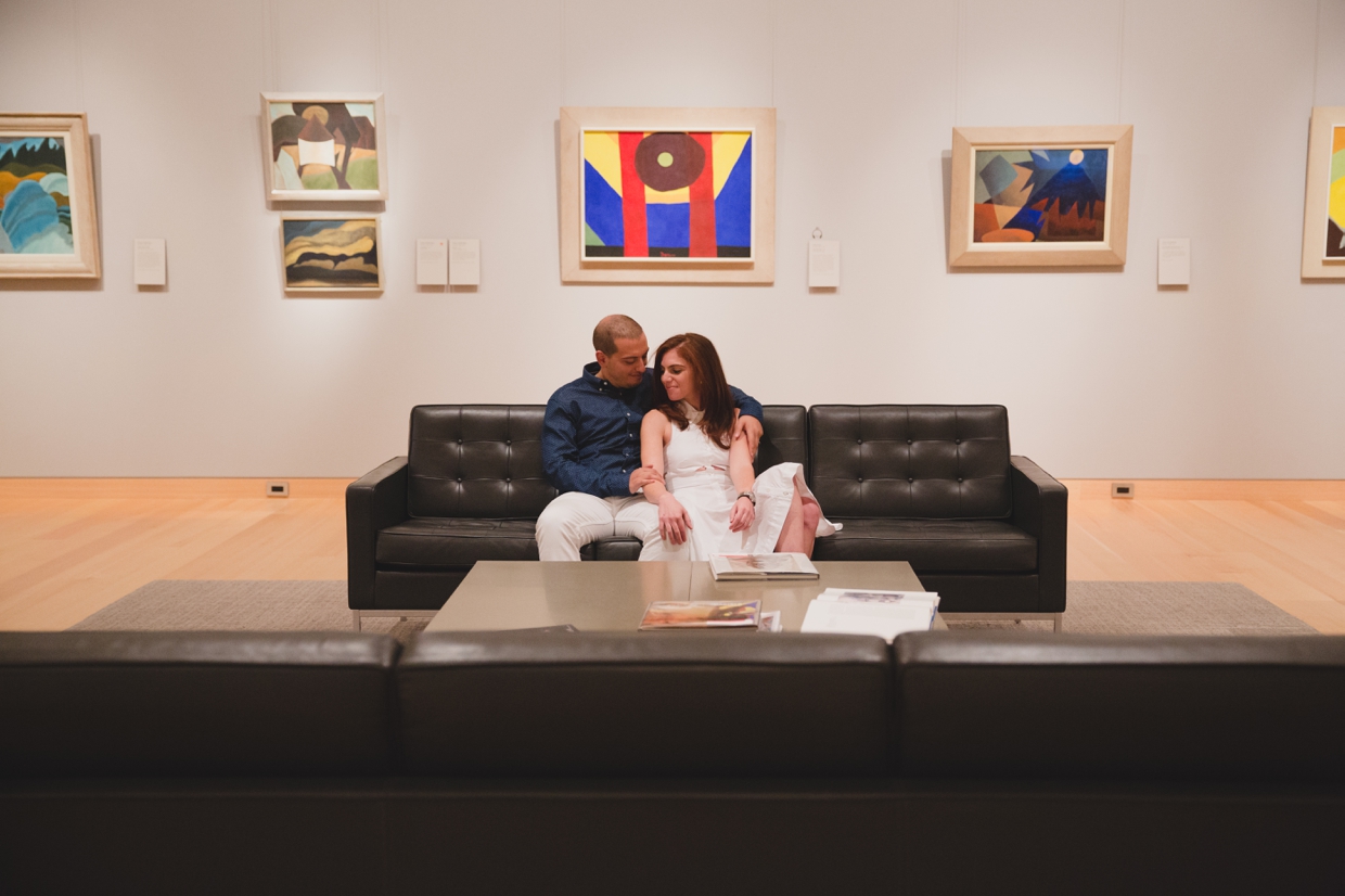 A couple sit on the couch together during their engagement session at the Museum of Fine Arts in Boston