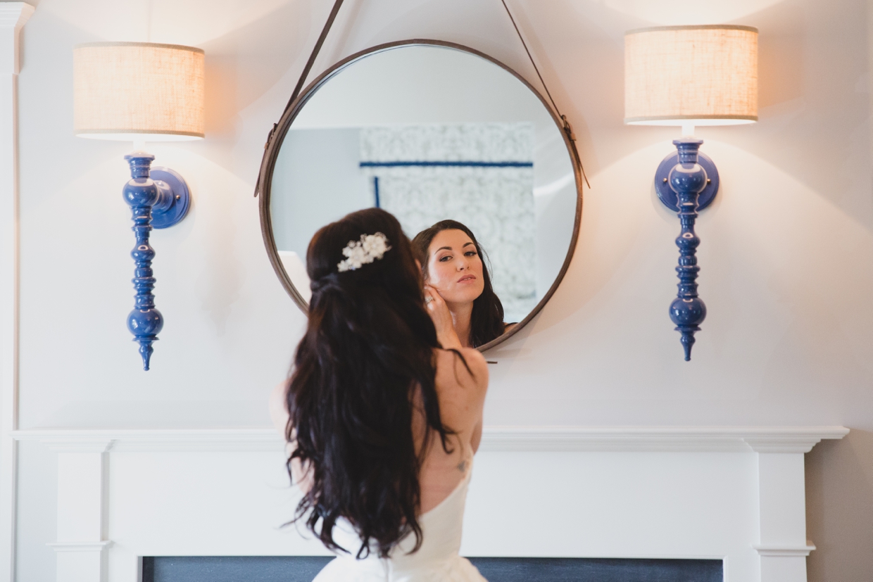 A bride looks in the mirror and puts on her earrings before her backyard wedding in Massachusetts