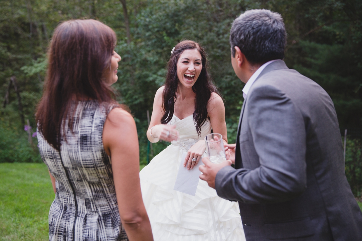 A bride laughs with friends during the cocktail hour of her backyard wedding ceremony in Massachusetts