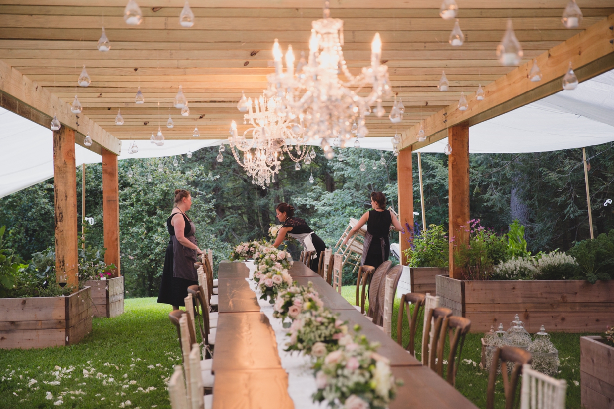 A behind the scenes photograph of Saltbox Fams setting the table at a backyard wedding in Massachusetts
