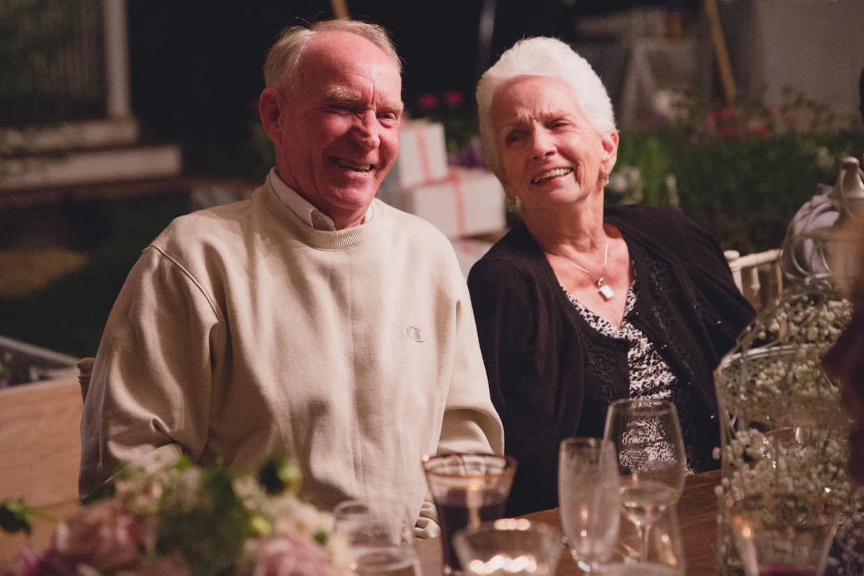 A sweet photograph of grandparents laughing during the dinner portion of a backyard wedding in Massachusetts