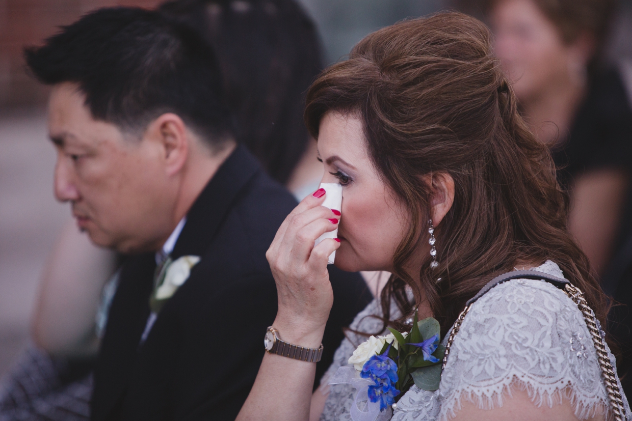An emotional photograph of the mother of the groom wiping away a tear during her son's wedding ceremony at the Boston Marriott Hotel