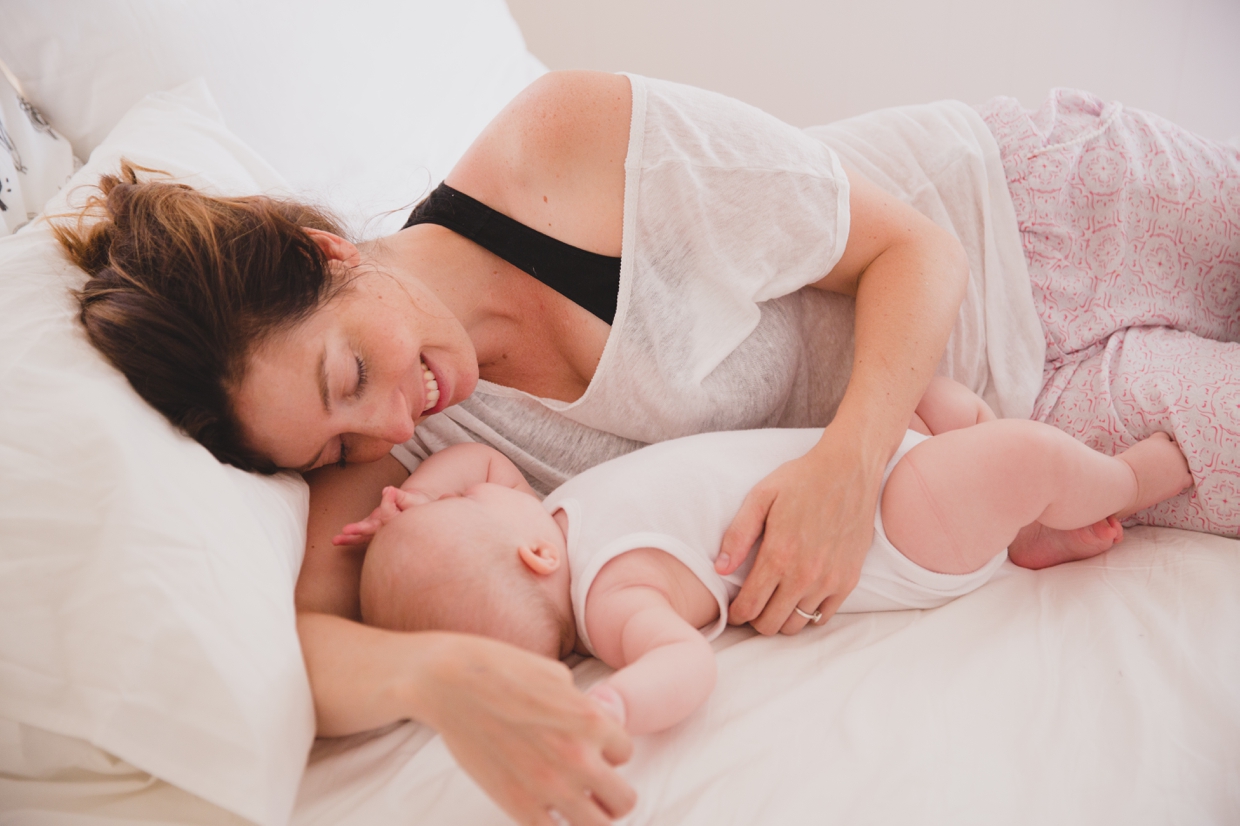 An intimate photograph of a mother laying with her baby during an in home family photo session in Boston