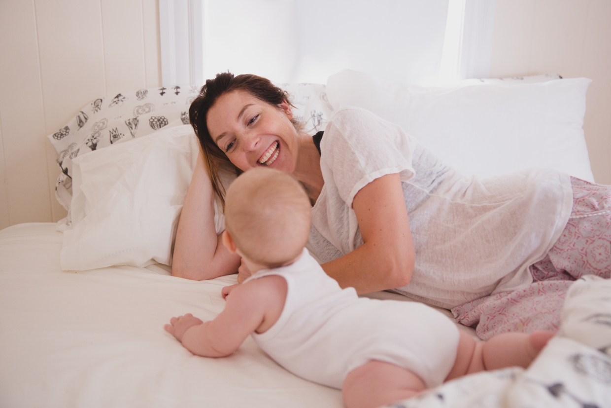 A sweet and intimate photograph of a mother and baby laughing in bed during an in home family photo session in Boston